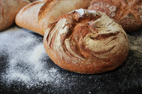 Auswahl an frischem Brot auf schwarzem Hintergrund. frisch gebackener hausgemachter Brotlaib auf rustikalem dunklen Hintergrund. — Stockfoto
