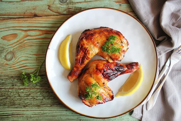 Gegrillte Hähnchenkeule mit knuspriger goldbrauner Haut, Zitrone, Petersilie auf weißem Teller auf dunklen Holzbrettern. Lebensmittel-Hintergrund. Ansicht von oben — Stockfoto