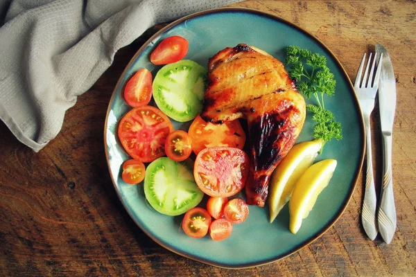 Quartos de perna de frango grelhados com pele marrom dourada crocante, tomate, limão em placas de madeira escura. Fundo alimentar. Vista superior — Fotografia de Stock