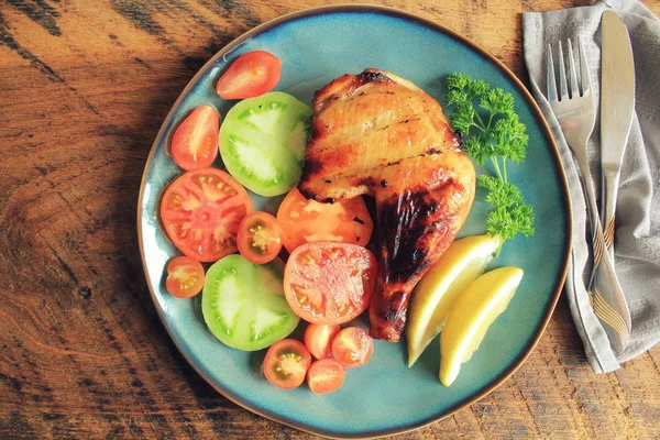 Grilled chicken leg quarters with crispy golden brown skin, tomatoe ,lemon on dark wooden boards. Food background. Top view — Stock Photo, Image