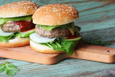 Biftek, soğan, salatalık, marul, peynir, ıspanak ve baharatlı ev yapımı hamburger. Tahta kesme tahtasına yakın taze hamburger.