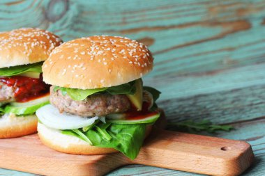 Biftek, soğan, salatalık, marul, peynir, ıspanak ve baharatlı ev yapımı hamburger. Tahta kesme tahtasına yakın taze hamburger. .