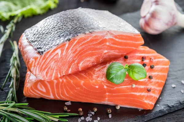 Siyah kesme tahtasında taze somon filetosu otlar ve baharatlarla.