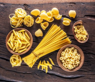Different pasta types on the wooden table. Top view. clipart