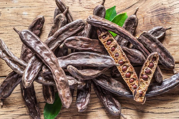 Johannisbrotschoten Und Johannisbrotbohnen Auf Dem Holztisch — Stockfoto