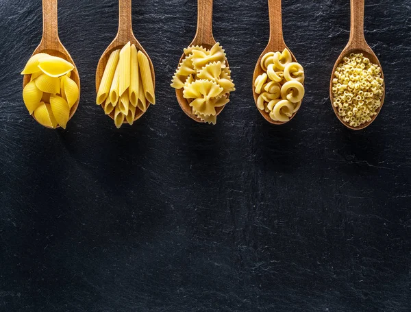 Masadaki tahta kaşıklarda farklı makarna tipleri. Üst görünüm.