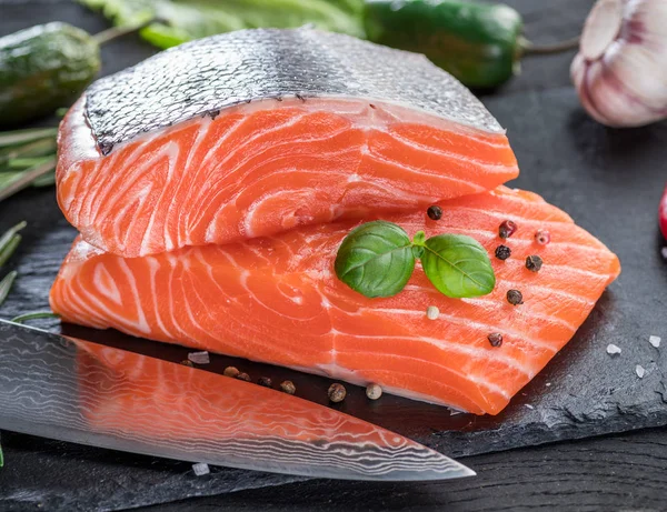 Siyah kesme tahtasında taze somon filetosu otlar ve baharatlarla.