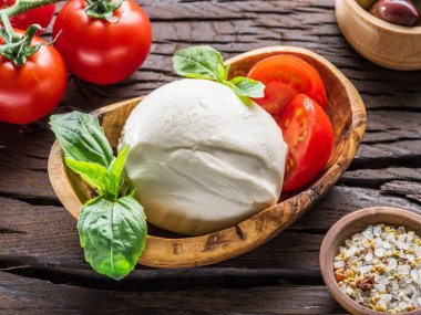 Buffalo mozzarella in the wooden bowl and cherry tomatoes on the table. clipart