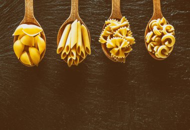 Masadaki tahta kaşıklarda farklı makarna tipleri. Üst görünüm.