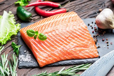 Otlar ve baharatlar ile siyah kesme tahtası üzerinde taze somon fileto.