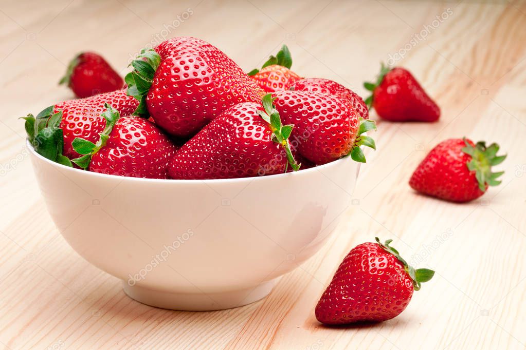 Strawberries in the bowl on wooden table.