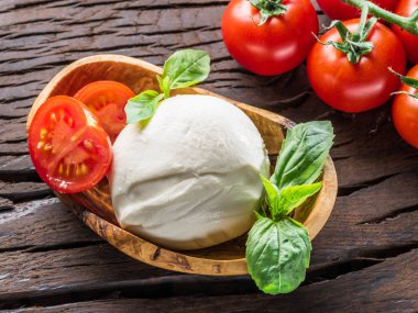 Buffalo mozzarella in the wooden bowl and cherry tomatoes on the table. clipart