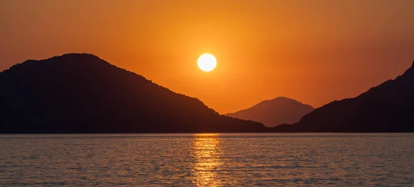 美丽的日落在海滨 太阳在石头后面落下 在水面上留下阳光的小路 — 图库照片