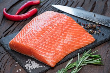 Otlar ve baharatlar ile siyah kesme tahtası üzerinde taze somon fileto.