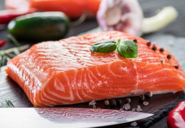 Siyah kesme tahtasında taze somon filetosu otlar ve baharatlarla.