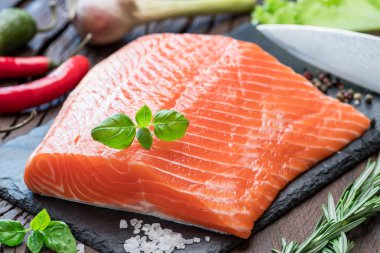 Otlar ve baharatlar ile siyah kesme tahtası üzerinde taze somon fileto.