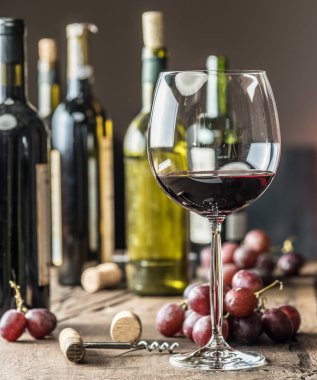 Bir bardak kırmızı şarap masanın üzerinde. Şarap şişesi ve arka plan, üzüm.