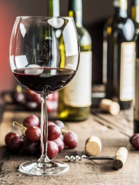 Bir bardak kırmızı şarap masanın üzerinde. Şarap şişesi ve arka plan, üzüm.