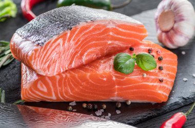 Siyah kesme tahtasında taze somon filetosu otlar ve baharatlarla.