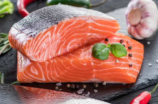 Siyah kesme tahtasında taze somon filetosu otlar ve baharatlarla.
