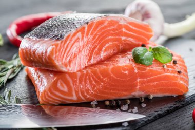 Siyah kesme tahtasında taze somon filetosu otlar ve baharatlarla.