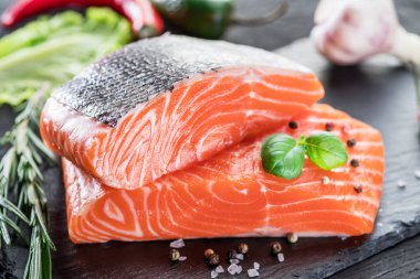 Siyah kesme tahtasında taze somon filetosu otlar ve baharatlarla.