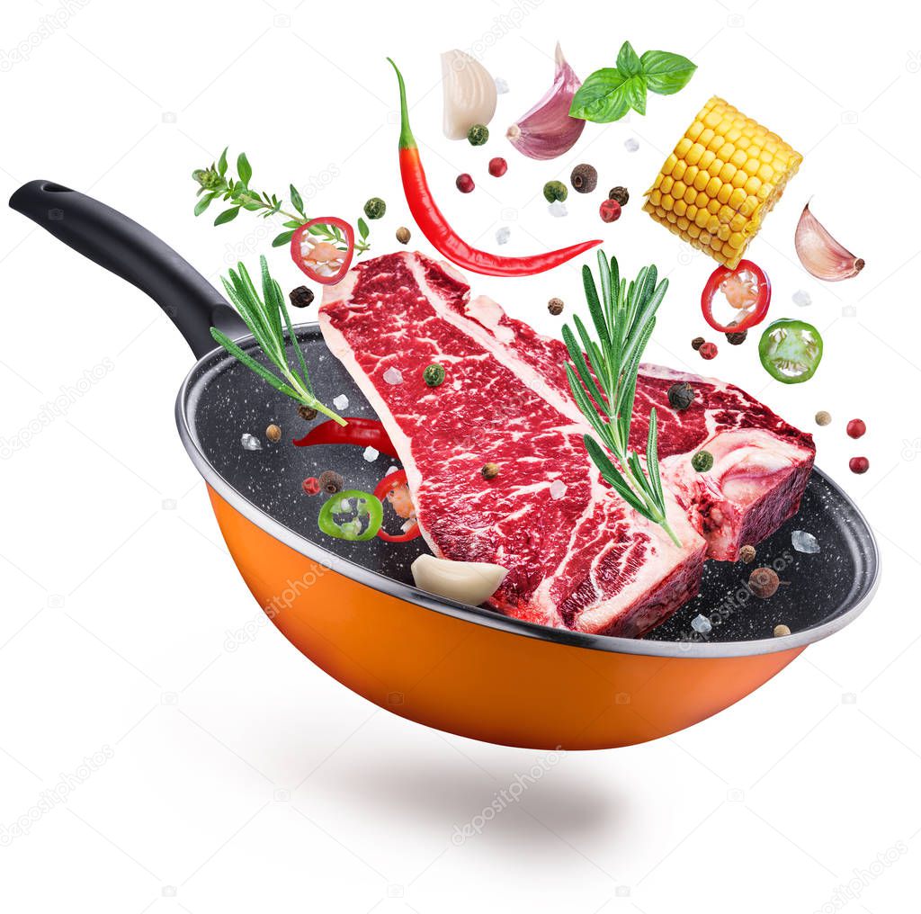 Flying T-bone steak and spices over a frying pan. File contains clipping path. Flying motion effect.