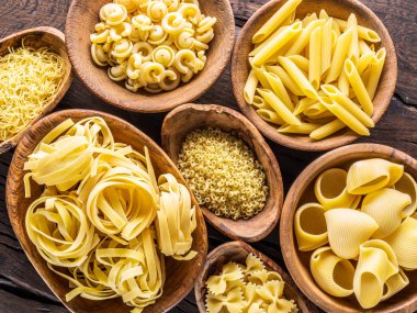 Different pasta types in wooden bowls on the table. Top view. clipart