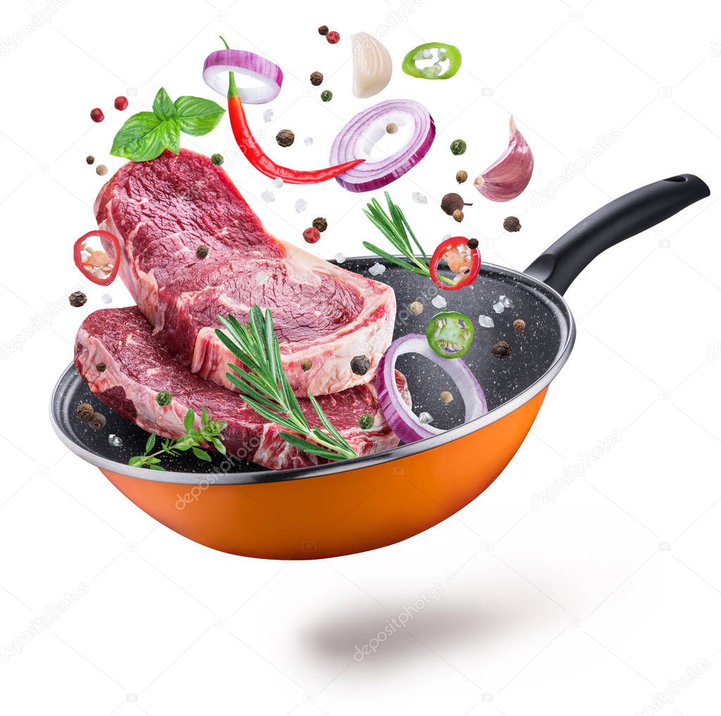 Flying meat steaks and spices over a frying pan. File contains clipping path. Flying motion effect.