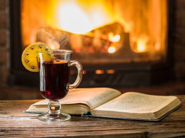 Sıcak mulled şarap ve ahşap masa üzerine bir kitap. Şömine ile arka planda sıcak ateş.