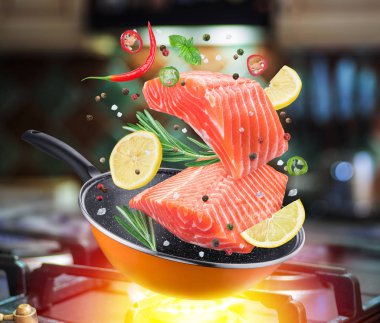 Uçan somon steak ve baharat bir kızartma tavası düşüyor. Pişirme işlemi uçan hareket etkisi. Gaz-soba, arka.