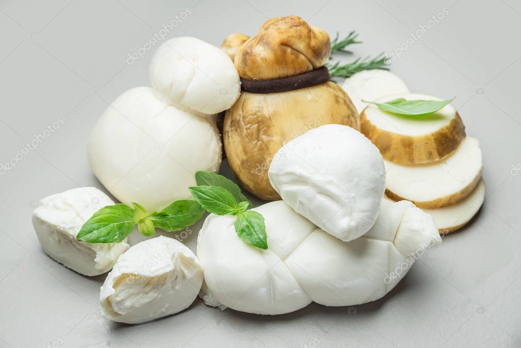 Mozzarella and Scamorza, traditional Italian cheeses with fresh herbs on gray background.