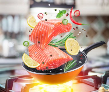 Uçan somon steak ve baharat bir kızartma tavası düşüyor. Pişirme işlemi uçan hareket etkisi. Gaz-soba, arka.