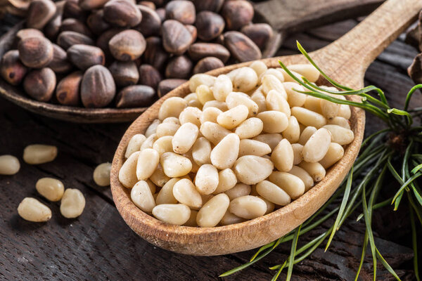 Pine nuts in the spoon and pine nut cone on the wooden table. Organic food.