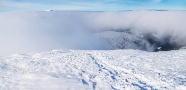 Beyaz ağır bulutların üstünde karla kaplı dağ başında.