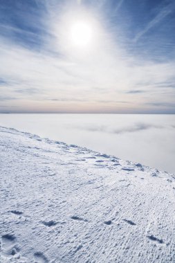 Dağ başında beyaz ağır bulutların üzerinde kar ile kaplı. Güneş ve mavi gökyüzü arka plan.