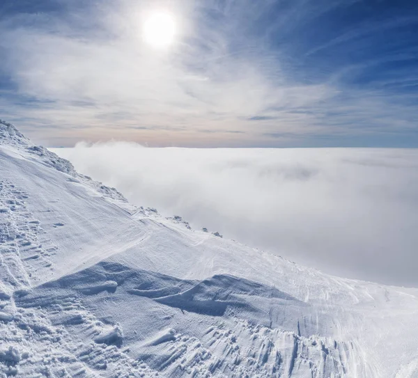 山のてっぺんは 白の重い雲の上の雪で覆われました 太陽と青い空 — ストック写真