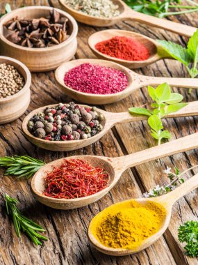 Ahşap masa üstünde tahta kaşıklar içinde renkli baharat çeşitleri.