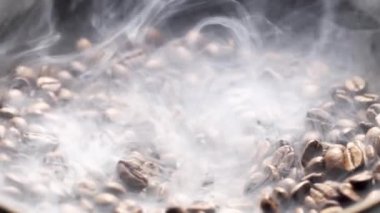 Kokulu kahve çekirdekleri kızartma tavasında kızartılır, duman kahve çekirdeklerinden gelir. Tüm kompozisyon kameranın etrafında yavaşça kayar..