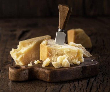 Tahtanın üzerinde bir parça parmesan peyniri ve peynir bıçağı. Koyu arkaplan.