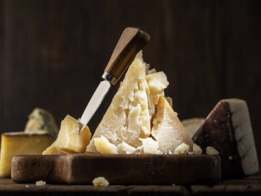 Tahtanın üzerinde bir parça parmesan peyniri ve peynir bıçağı. Koyu arkaplan.