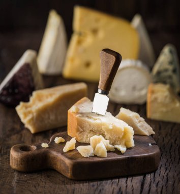 Parmesan peyniri ahşap tahta üzerinde parçası. Arka plan, farklı peynir çeşitleri.