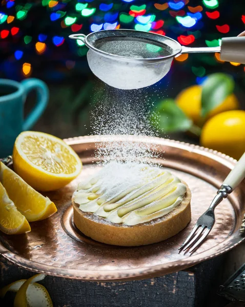 Lemon tart. Cooking of lemon dessert. Sugar powder is sprinkled on top through a strainer. Blurred heart festive background.