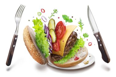 Hamburger malzemeler ve çatal bıçak takımı havada asılı. Renkli c