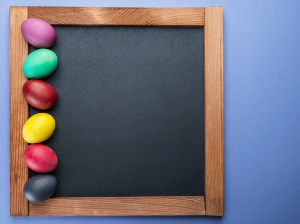 Blackboard and colorful Easter eggs around it. View from above. — Stock Photo, Image