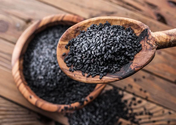 Semillas de sésamo negro en la cuchara de madera. Antigua mesa de madera y dis — Foto de Stock