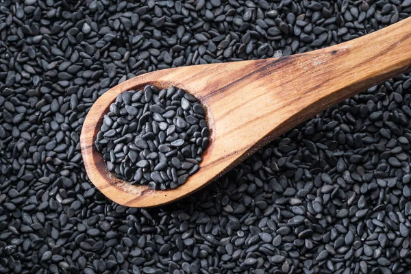 Semillas de sésamo negro en la cuchara de madera. Semillas de sésamo en el plato — Foto de Stock