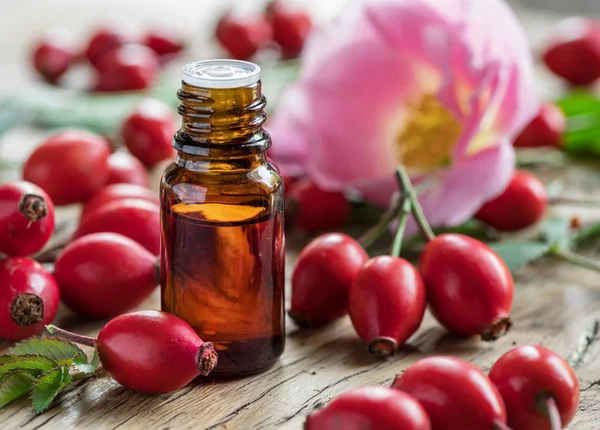 Rose-hips and rose hip seed oil on the wooden table. — Stock Photo, Image