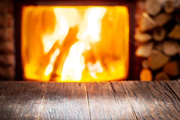 Empty wooden table and fireplace with warm fire at the backgroun — Stock Photo, Image