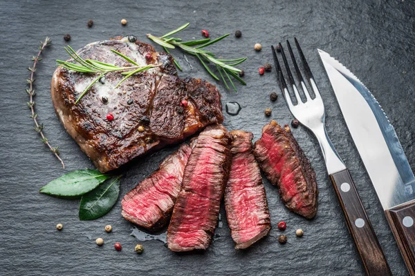 Středně vzácný steak z Ribeye s bylinkami na grafitové desce. — Stock fotografie